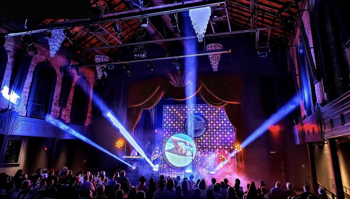A packed venue with beam lighting and an LED video wall behind the stage